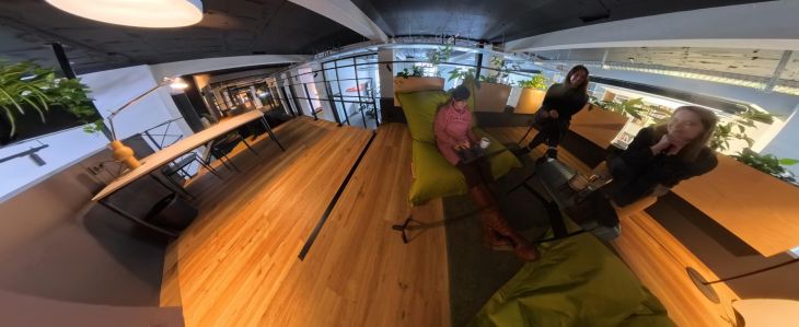 Drei Frauen in einem modernen Coworking-Space mit Holzboden, grünen Sitzsäcken und Pflanzen.