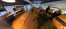 Drei Frauen in einem modernen Coworking-Space mit Holzboden, grünen Sitzsäcken und Pflanzen.